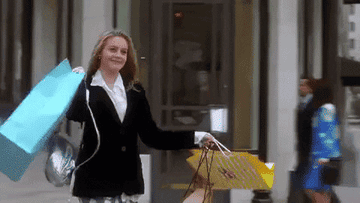 Cher from clueless walking out of a store carrying tons of shopping bags