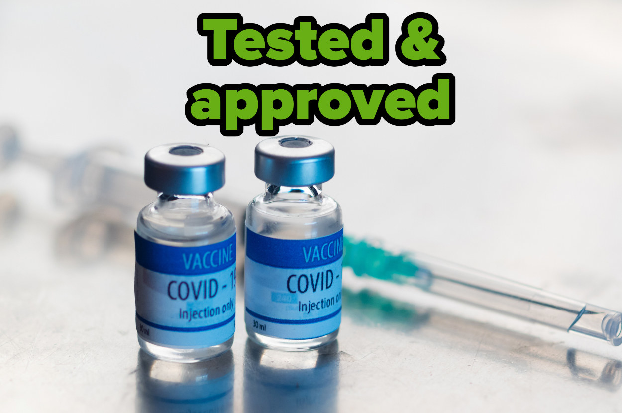 Two vials of the COVID-19 vaccine and a needle sit on a table. Above them sits the words &quot;tested and approved&quot;