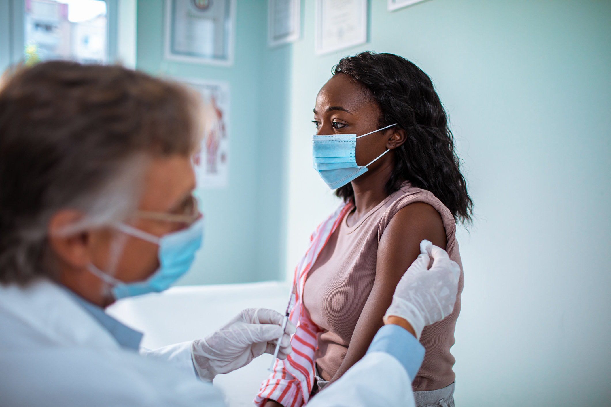 A woman receives a vaccination in a medical setting. She is wearing a mask.