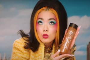 rina sawayama wears a lot of makeup and a furry jacket, looking upward, mouth in kiss position