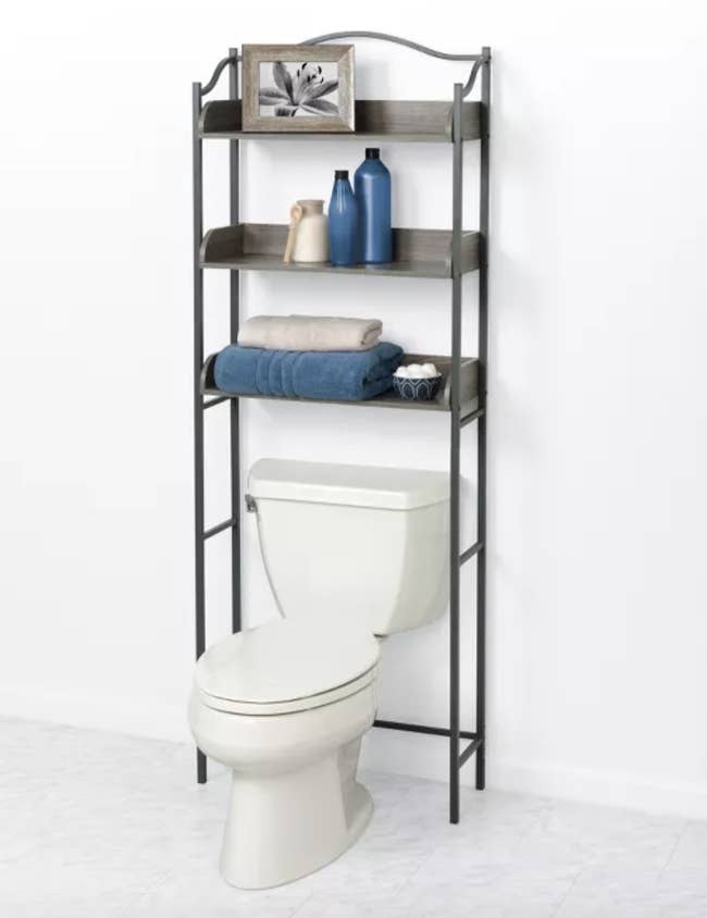brown storage unit with three shelves above white toilet