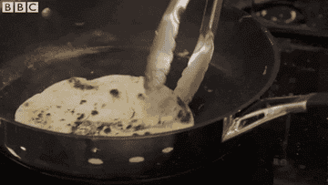 Tongs flipping a tortilla in a smoky pan