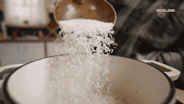 Rice being poured from a wooden bowl into a dutch oven