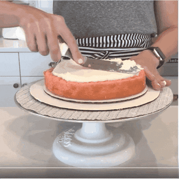 Someone icing a cake with an offset spatula while rotating the cake plate its on