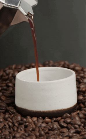 A French press pouring coffee into a small cup, sitting atop a layer of coffee beans