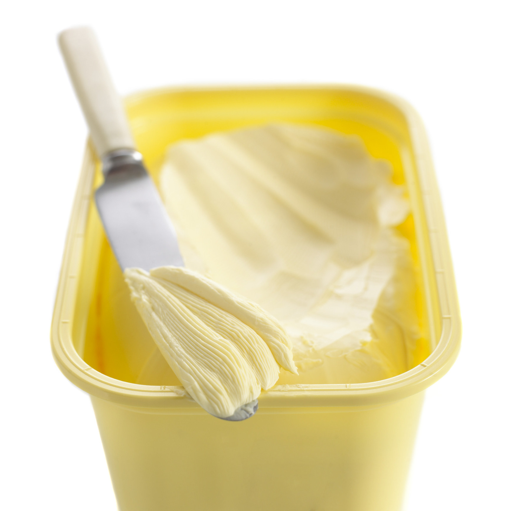 A butter knife with a smear of margarine on it sitting atop a rectangular tub of margarine