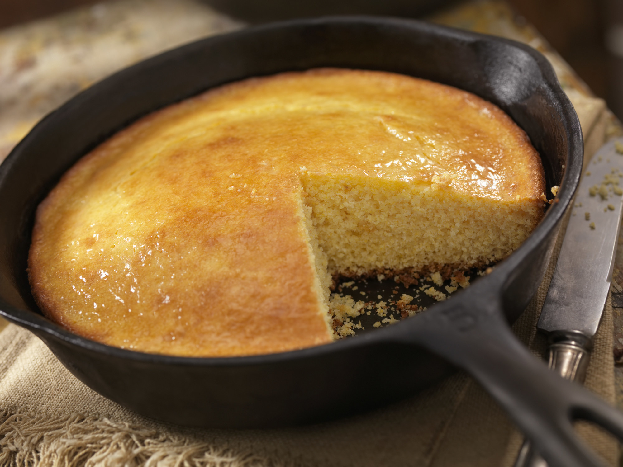 Cornbread in a cast iron pan with one slice taken out, knife by the pan