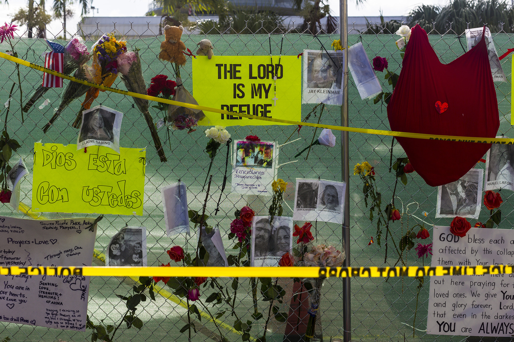 Flowers, posters and photos of people are shown behind police line tape