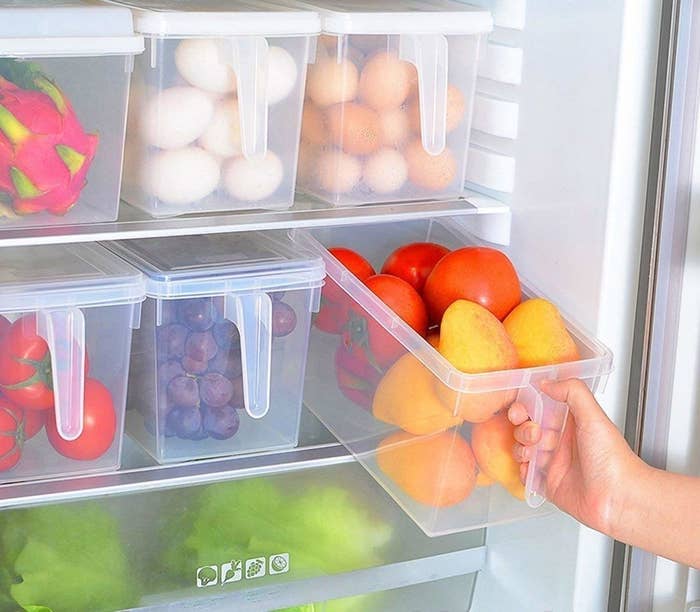 A fridge with 6 plastic storage containers with handle containing fruits and vegetables