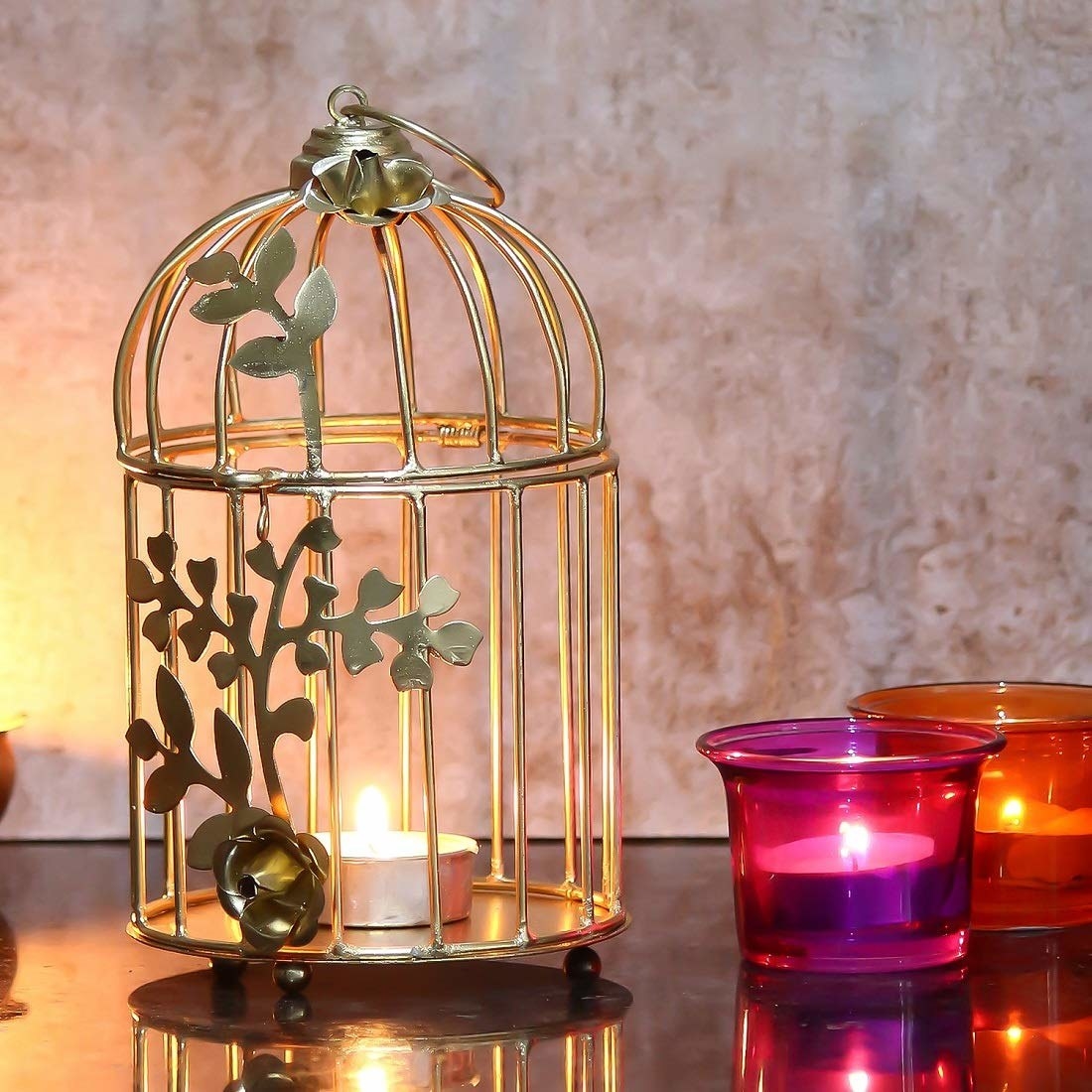 A golden birdcage with a tealight in it next to tealight holders with tealights