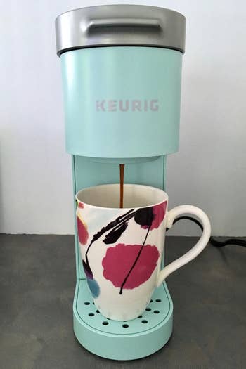 a reviewer photo of the Keurig in light blue with coffee dispensing into a mug 