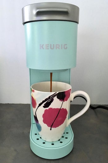 a reviewer photo of the Keurig in light blue with coffee dispensing into a mug 