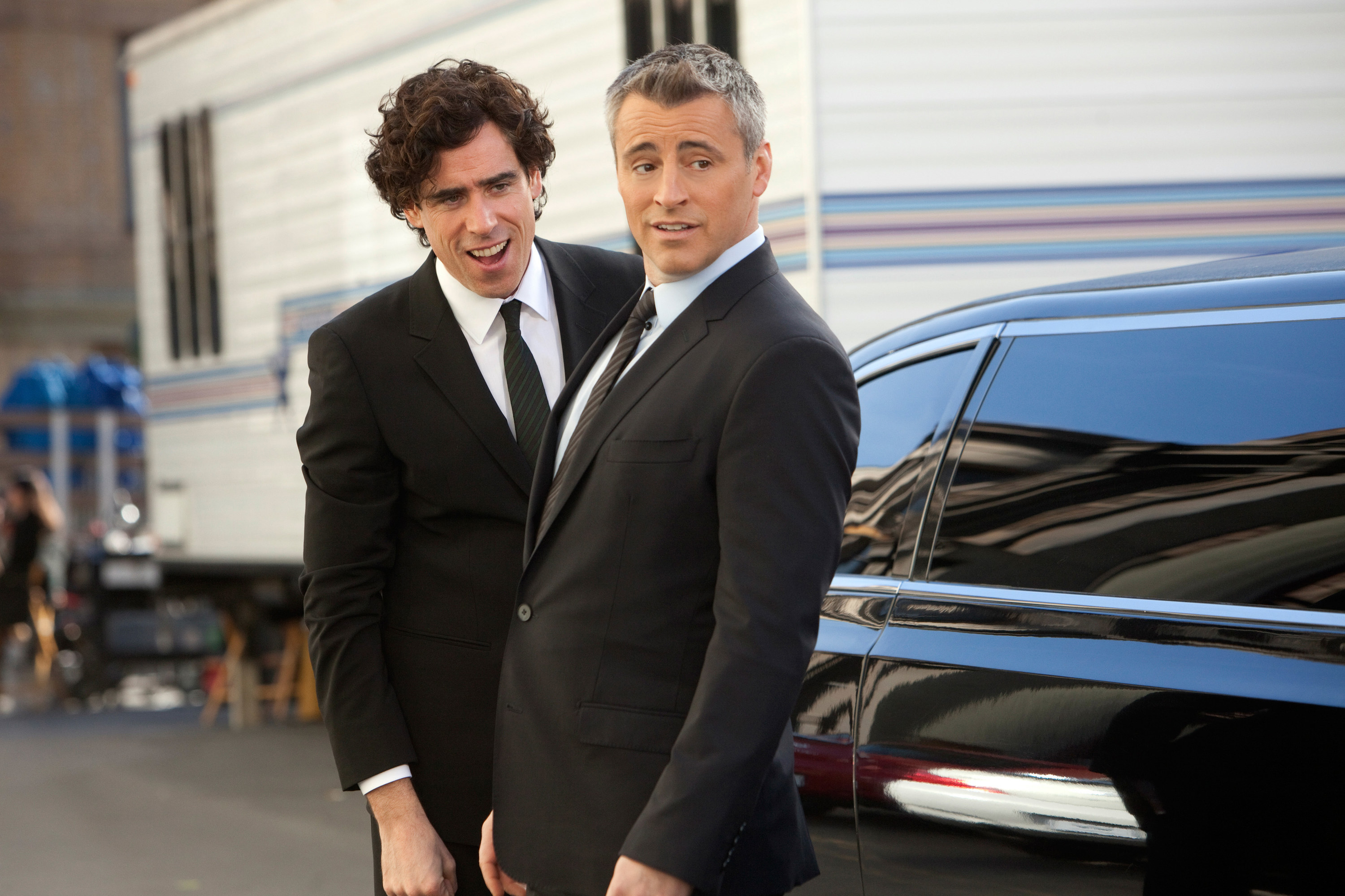 Stephen Mangan and Matt LeBlanc wearing suits and standing outside of a limo as Sean and Matt on &quot;Episodes&quot;