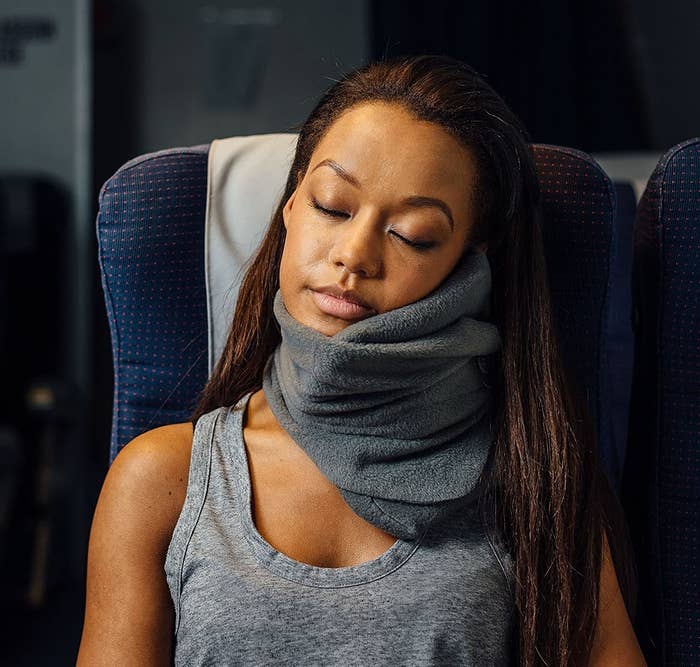model wearing a gray trtl pillow while sleeping on a plane