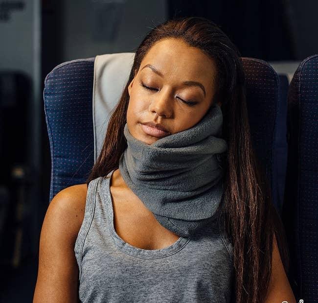 model wearing a gray trtl pillow while sleeping on a plane