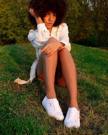 model wearing the Superga sneakers, sitting on a grassy hill