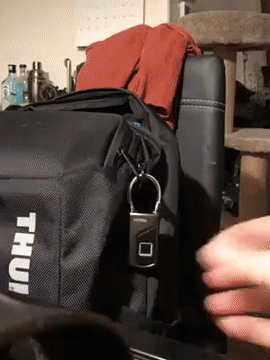Reviewer GIF showing them using their thumb to open the lock while attached to a backpack
