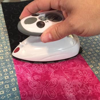 a reviewer photo of a hand using the iron on a strip of pink fabric 