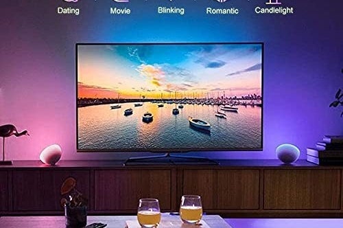 A TV in a living room being backlit with an LED strip. There are two glasses with drinks on a table in front of the TV
