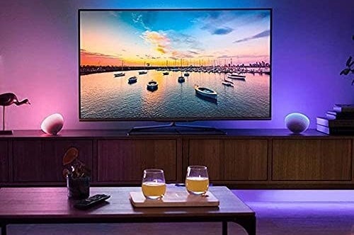 A TV in a living room being backlit with an LED strip. There are two glasses with drinks on a table in front of the TV.