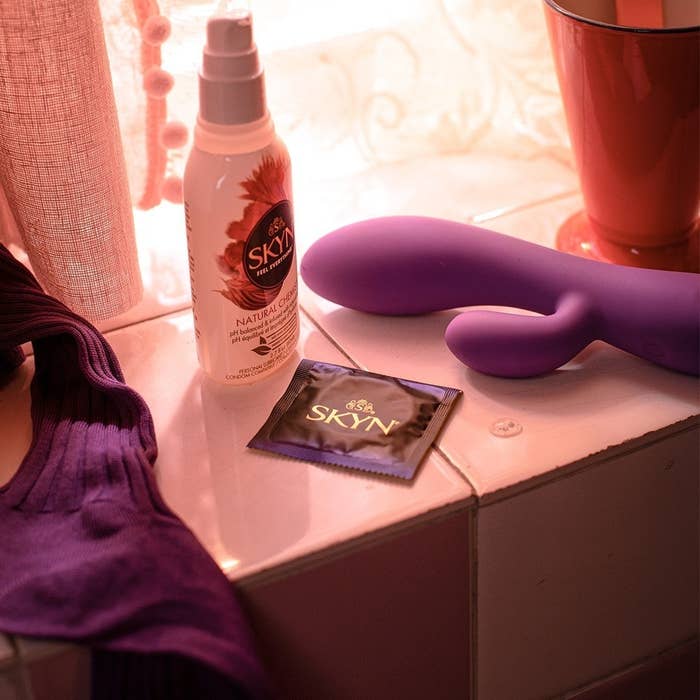 White bottle of lubricant, black and purple individual condom, and purple vibrator on counter