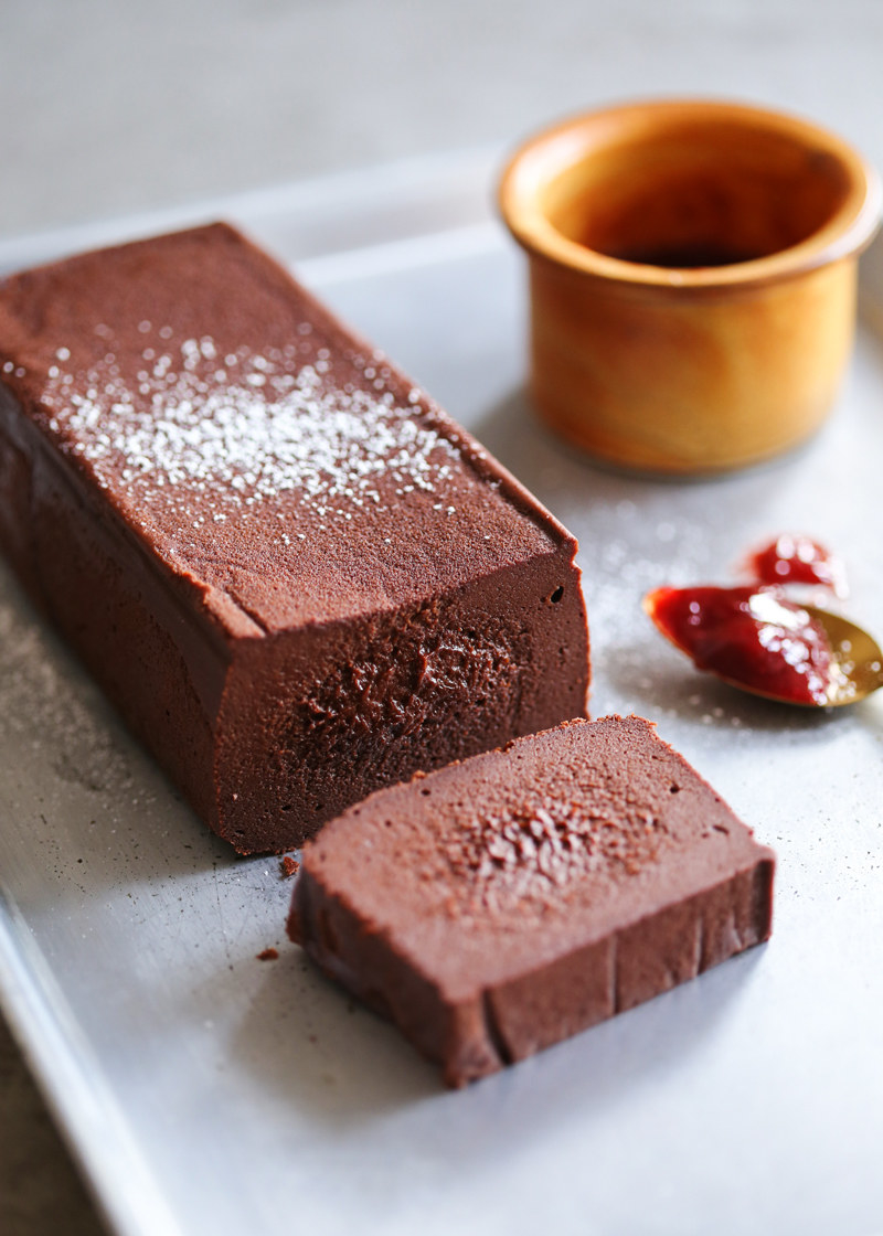 Long rectangular brick of chocolate terrine with one slice laying on its face.