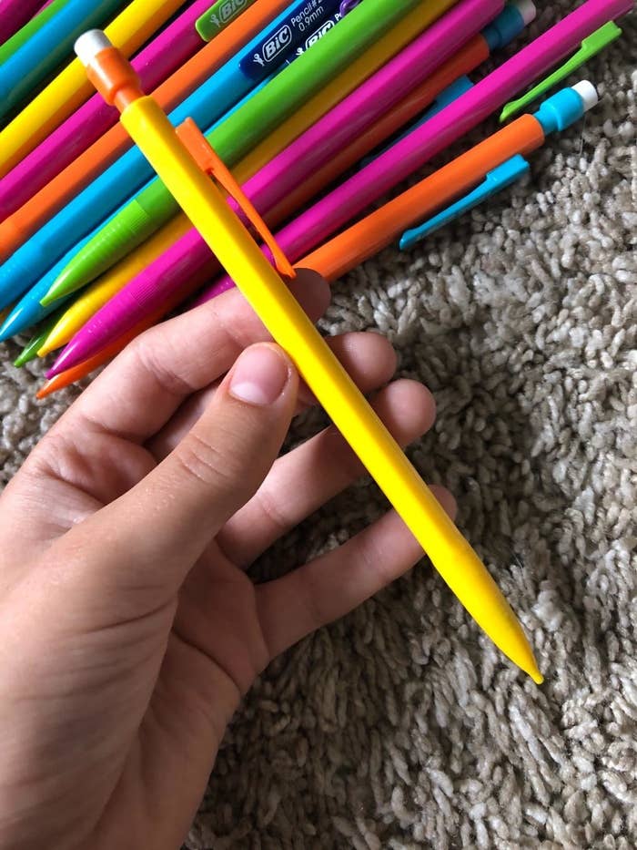 reviewer holding one of the pencils in yellow with the rest of the colored assortment in the background