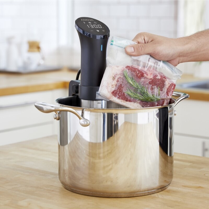 A person putting a bag of steak into a stainless steel pot; the sous vide device is submerged too