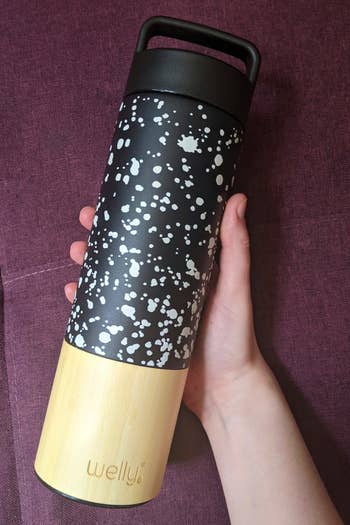 a hand holding a black and white water bottle with a bamboo bottom 