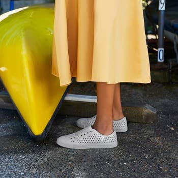 model wearing the white Native slip-ons with a yellow dress
