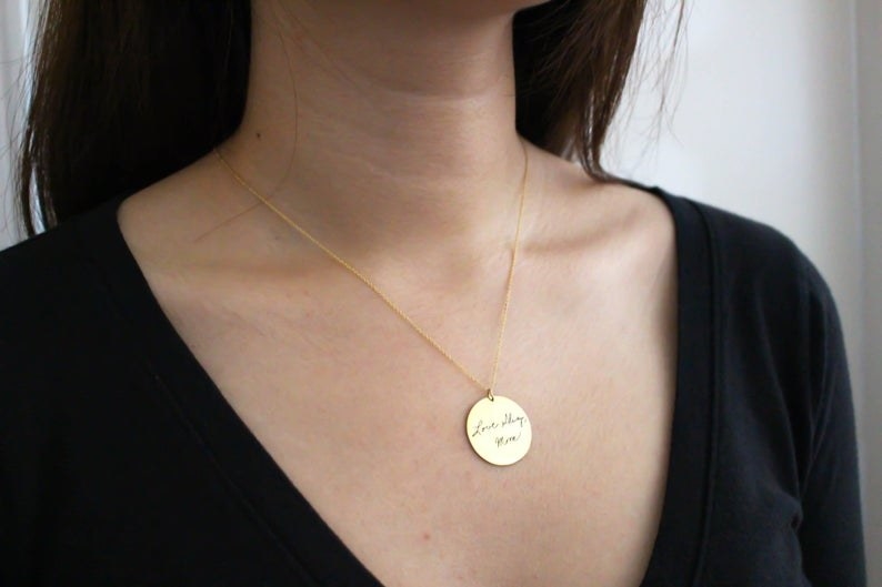 a model wearing the gold disc necklace with handwriting in the center