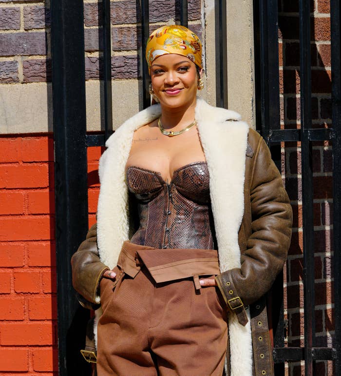 Rihanna with her hands in her pockets and wearing a snakeskin print bustier, coat and a silk bandanna