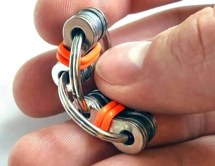 A person holding a metal fidget toy with orange pieces on it