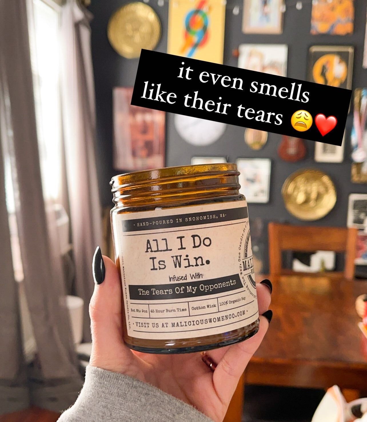 A person holding up a candle that says &quot;All I do is win, infused with the tears of my opponents&quot; and the words &quot;it even smells like their tears&quot; written on the image