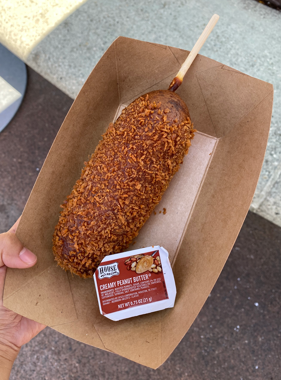A close-up image of the corn dog, which is deep fried and comes with a side dipping packet of creamy peanut butter