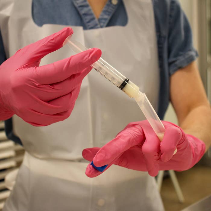 A gloved worker guides breast milk from a dropper into a test tube