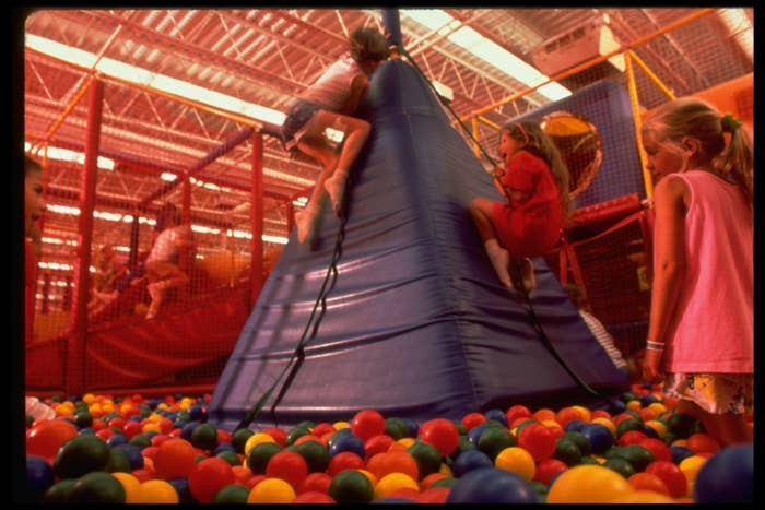 Children playing amid colorful plastic balls and on a big blue pyramid at a Discovery Zone children&#x27;s fitness center
