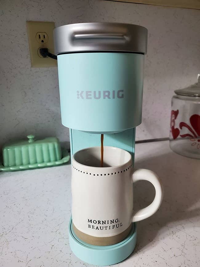 a reviewer photo of the keurig coffee maker with a coffee cup inside ready for the coffee to pour