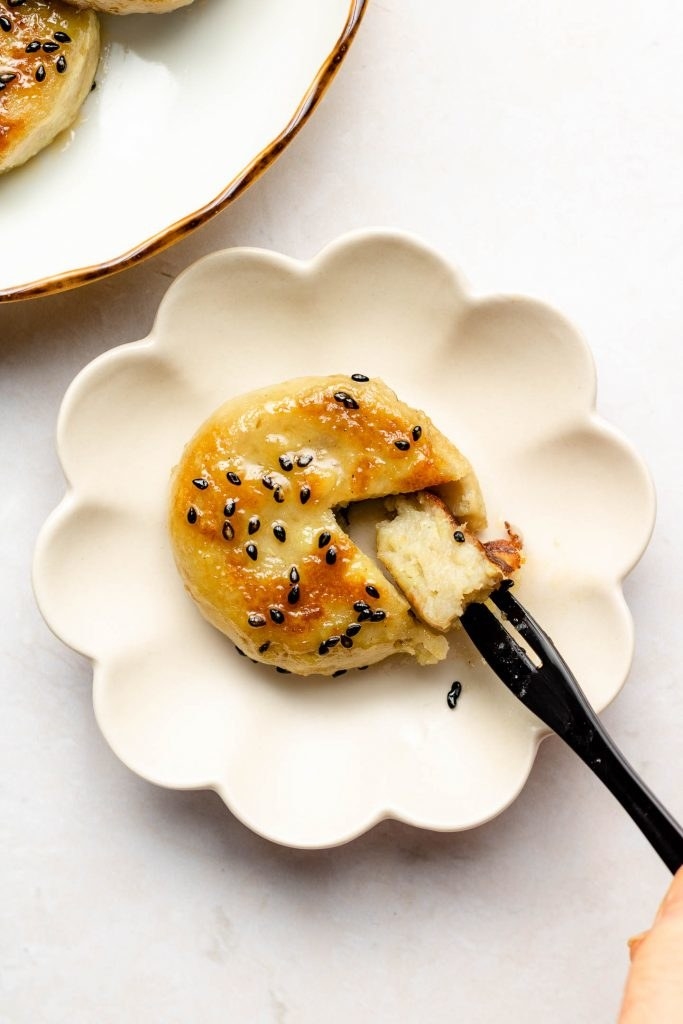 A fresh serving of sweet potato yaki mochi topped with black sesame seeds, with a fork pulling out a piece to show its dense core.
