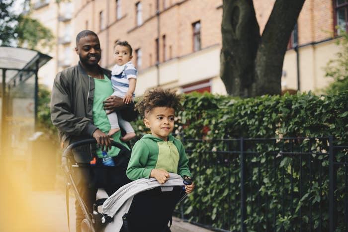 a man walking down the street carrying a baby with a toddler in a stroller