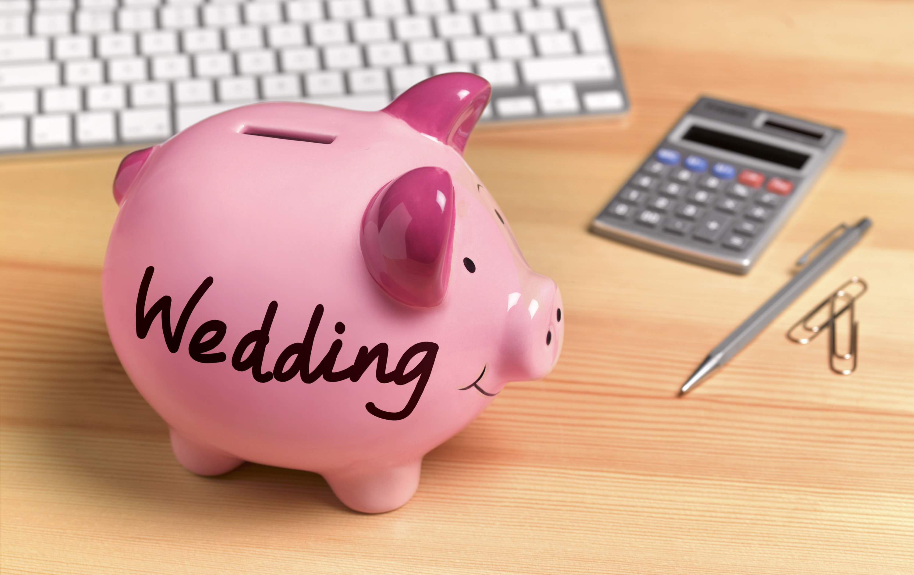 A piggy bank with the word &quot;Wedding&quot; written on the side next to a calculator and pen