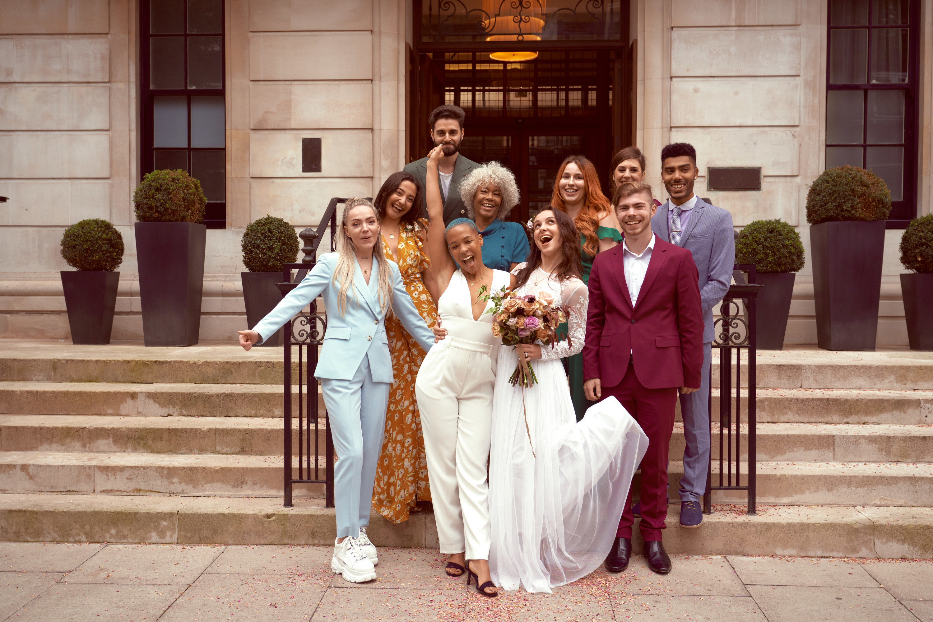 A wedding party of adults posing for a photo outside on steps