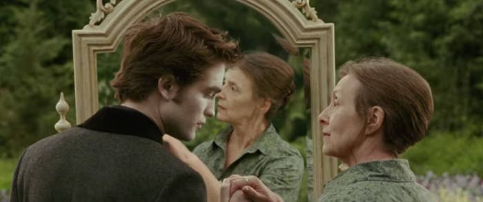 Edward and Bella stand outside in a field in front of a mirror, Edward, looking the same as always, but Bella appearing as an old lady