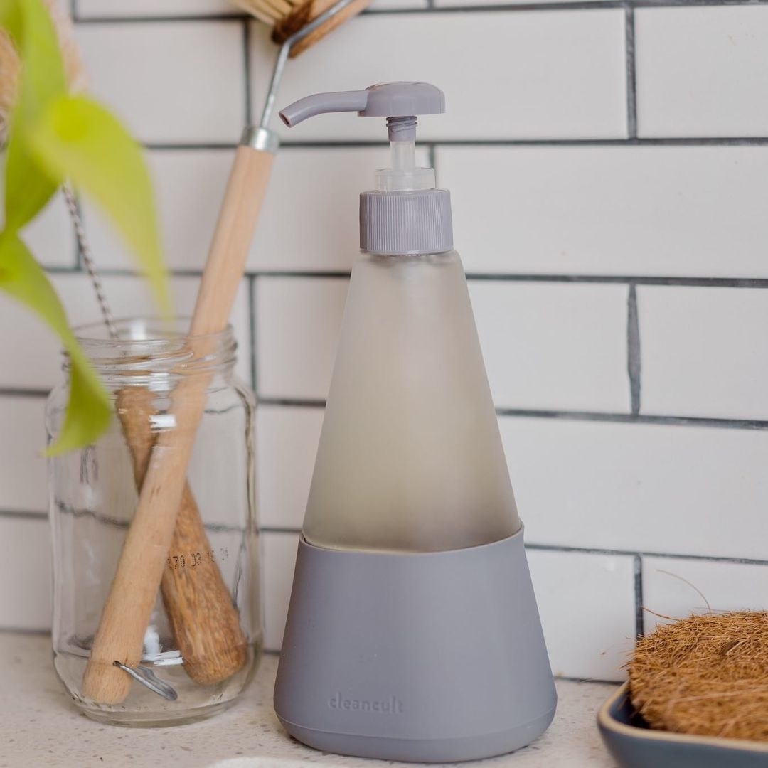 The pyramid-shaped glass soap dispenser next to cleaning brushes