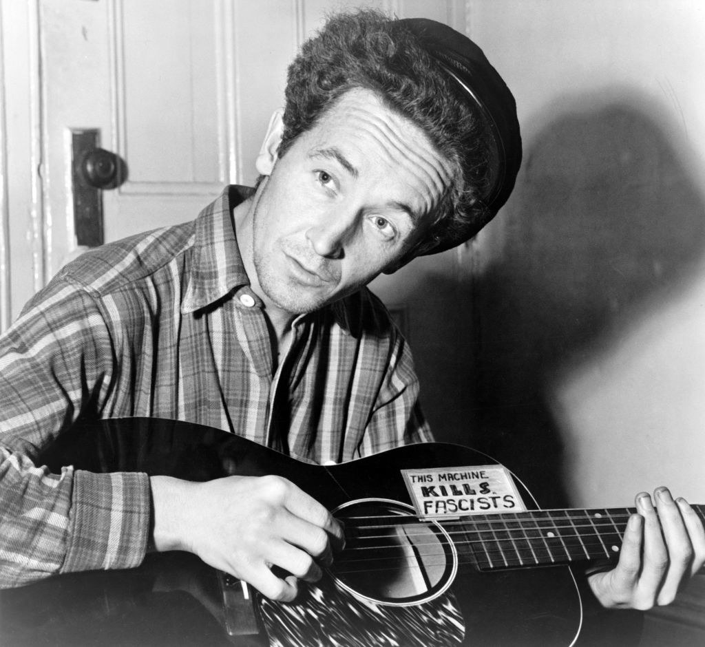 Woody Guthrie holding his &quot;this machine kills fascists&quot; guitar