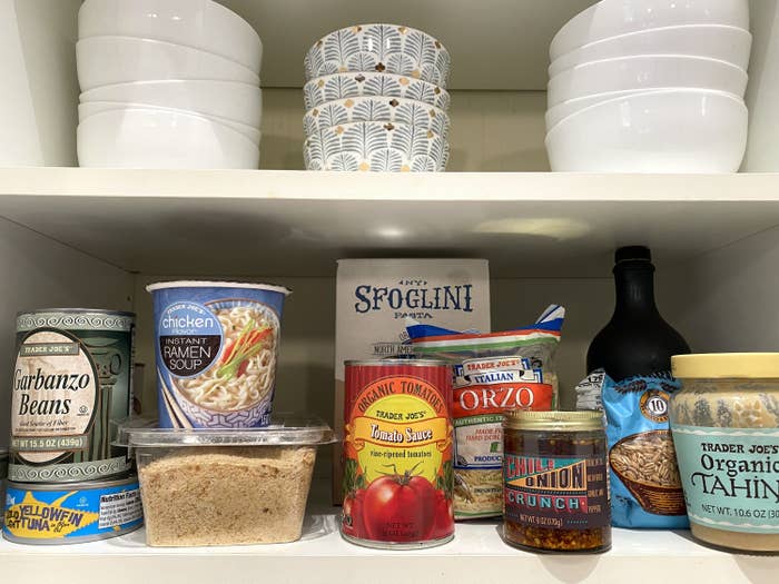 Cupboard shelves with foods like organic tahini, tomato sauce, orzo, and garbanzo beans