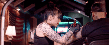 A GIF of a tattoo artist turning and giving a rock on sign with her hand