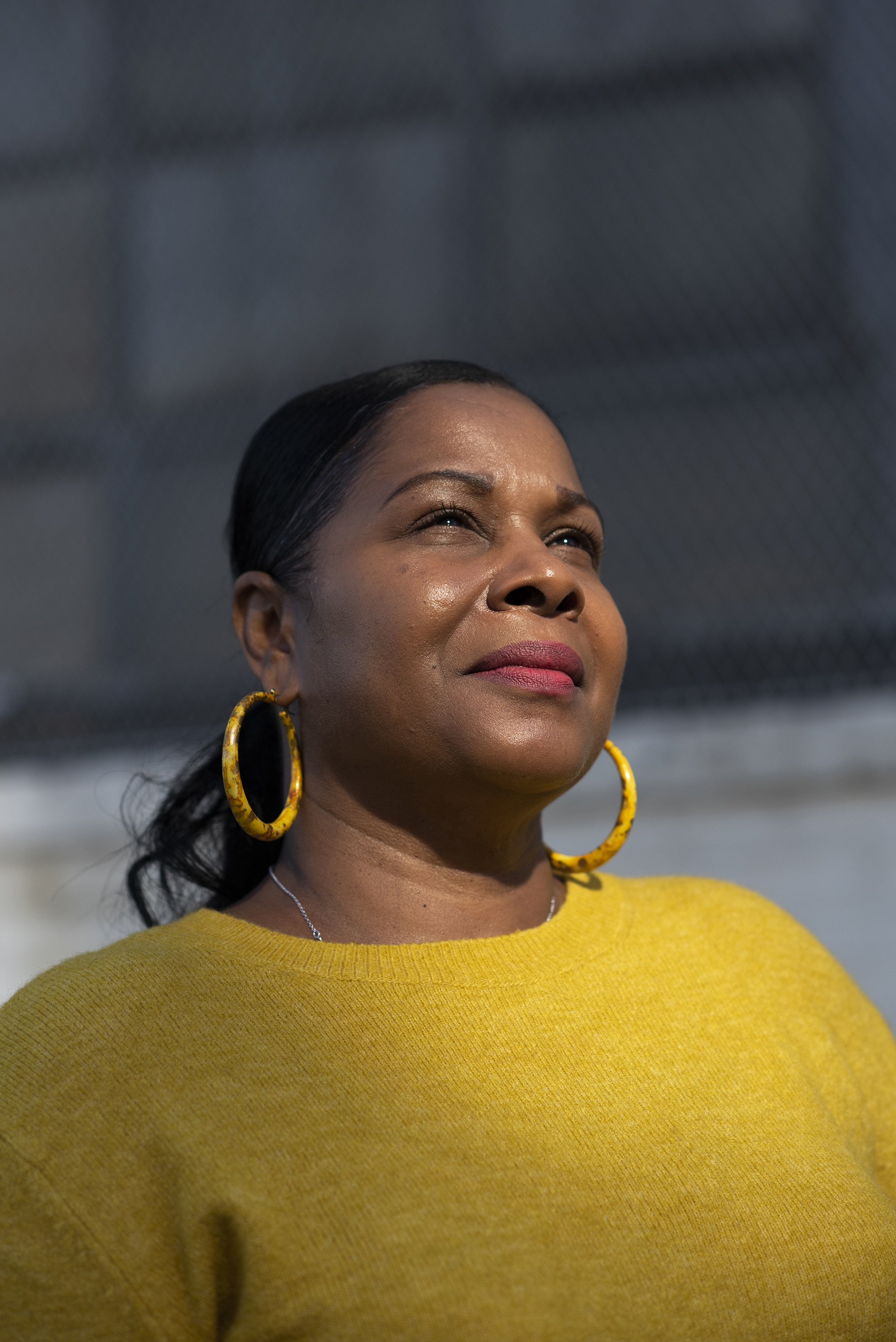 A woman in a sweater and matching hoop earrings faces into the sun