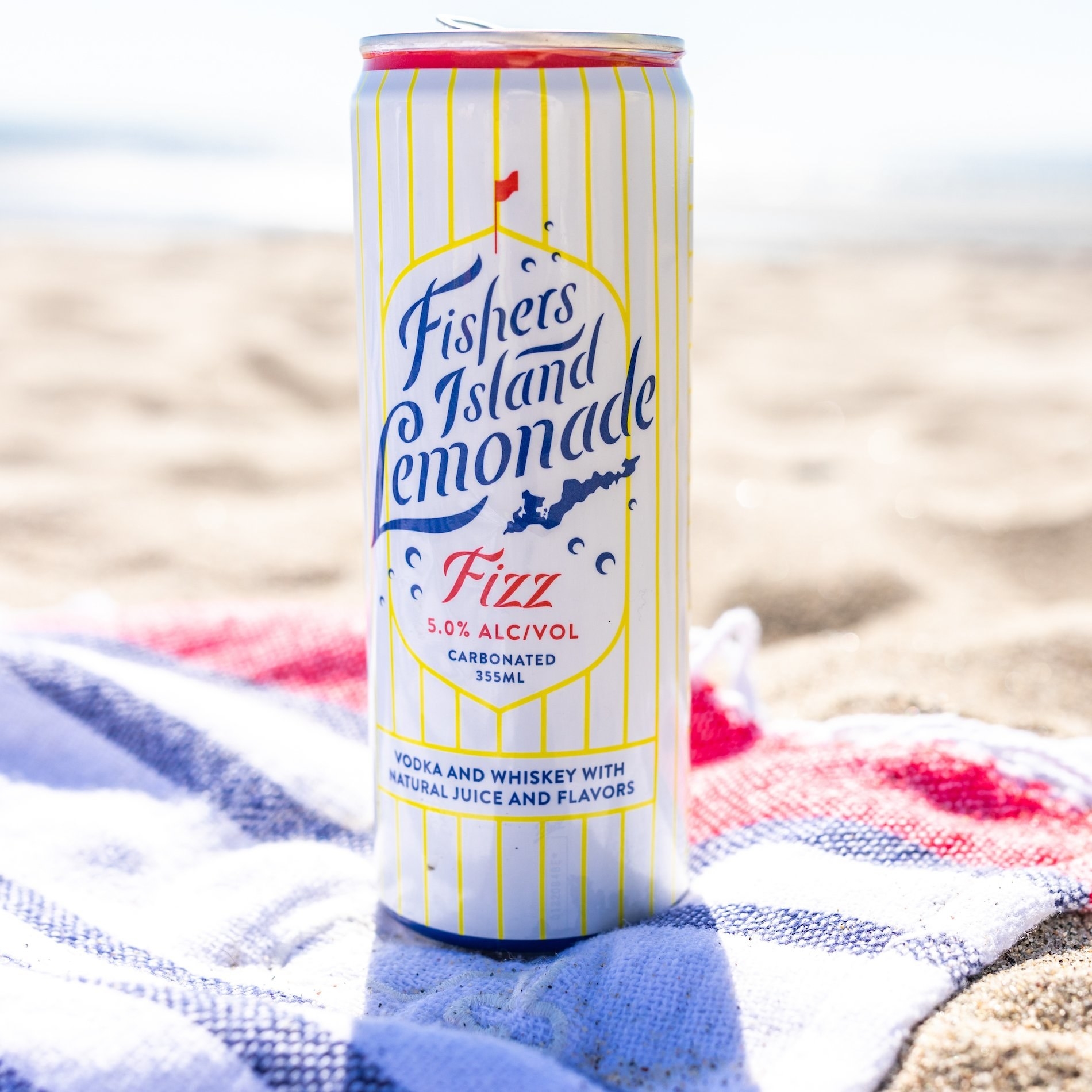 a can of fishers island lemonade fizz on a towel on a sandy beach