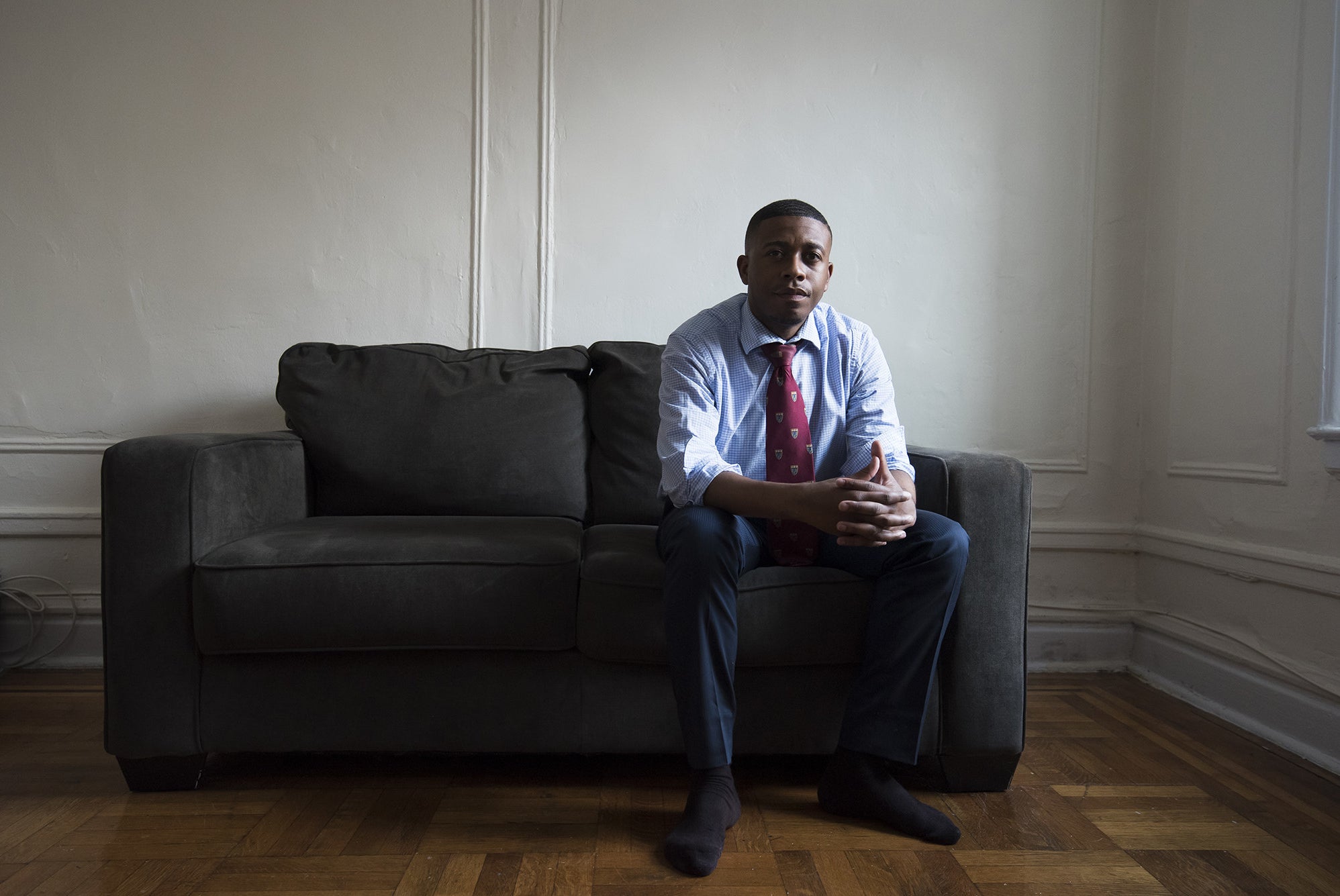 A man in a suit sits on a couch in an apartment